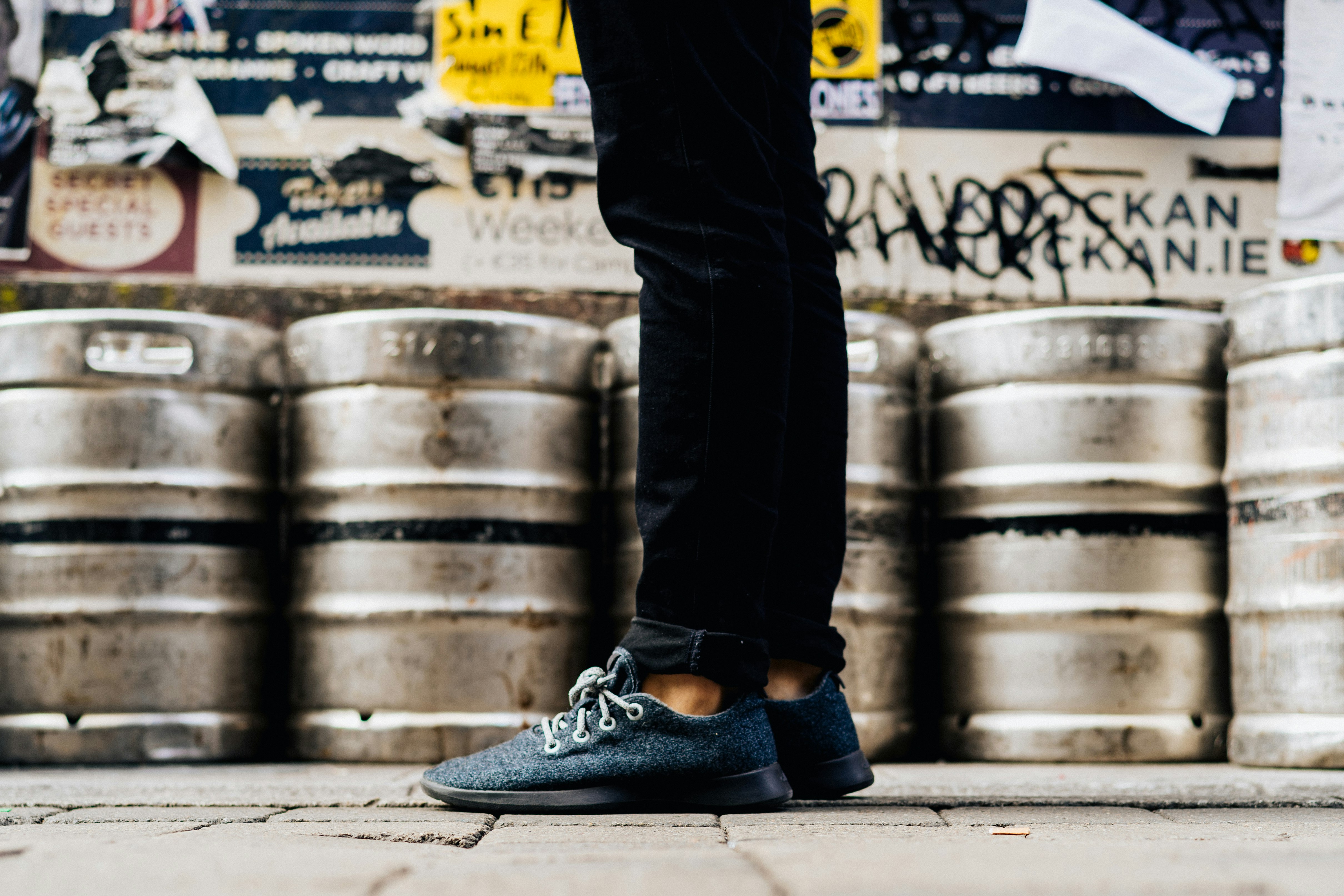 standing man wearing gray shoes beside cans